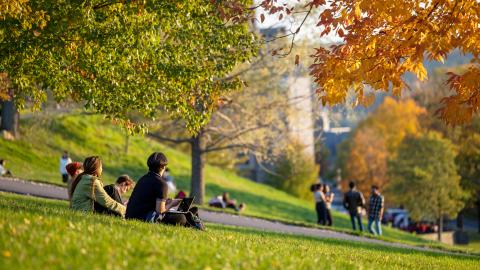 students sit on a campus slope in fall